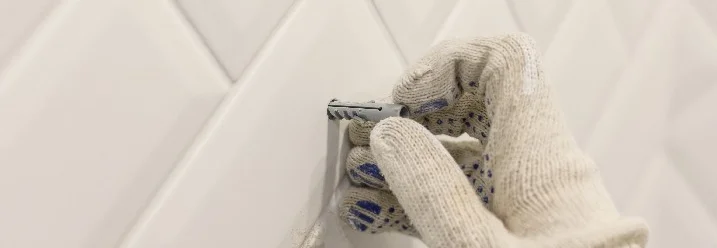 Hand in einem Arbeitshandschuh setzt einen Dübel in eine weiße Wand